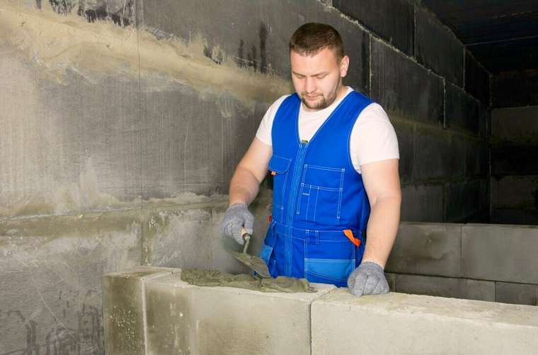 Albañil con chaleco azul trabajando sobre una pared de bloques