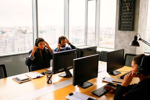 Operadores con auriculares trabajando frente a monitores junto a un ventanal