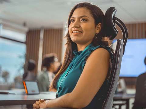 Mujer sonriendo en una oficina luminosa, sentada en una silla ergonómica
