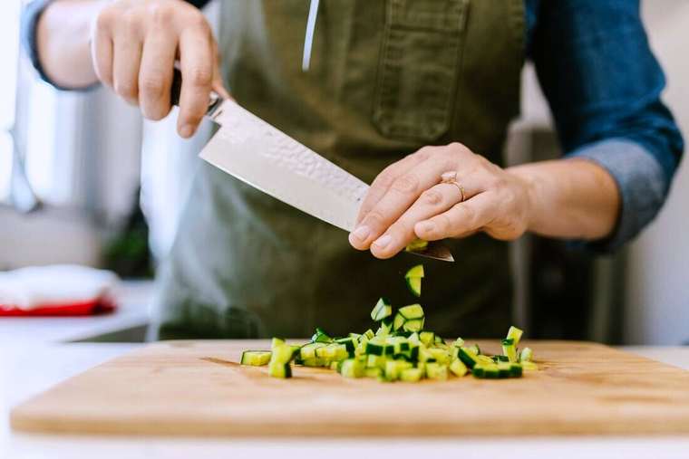 Manos cortando pepino sobre una tabla de madera con un cuchillo grande