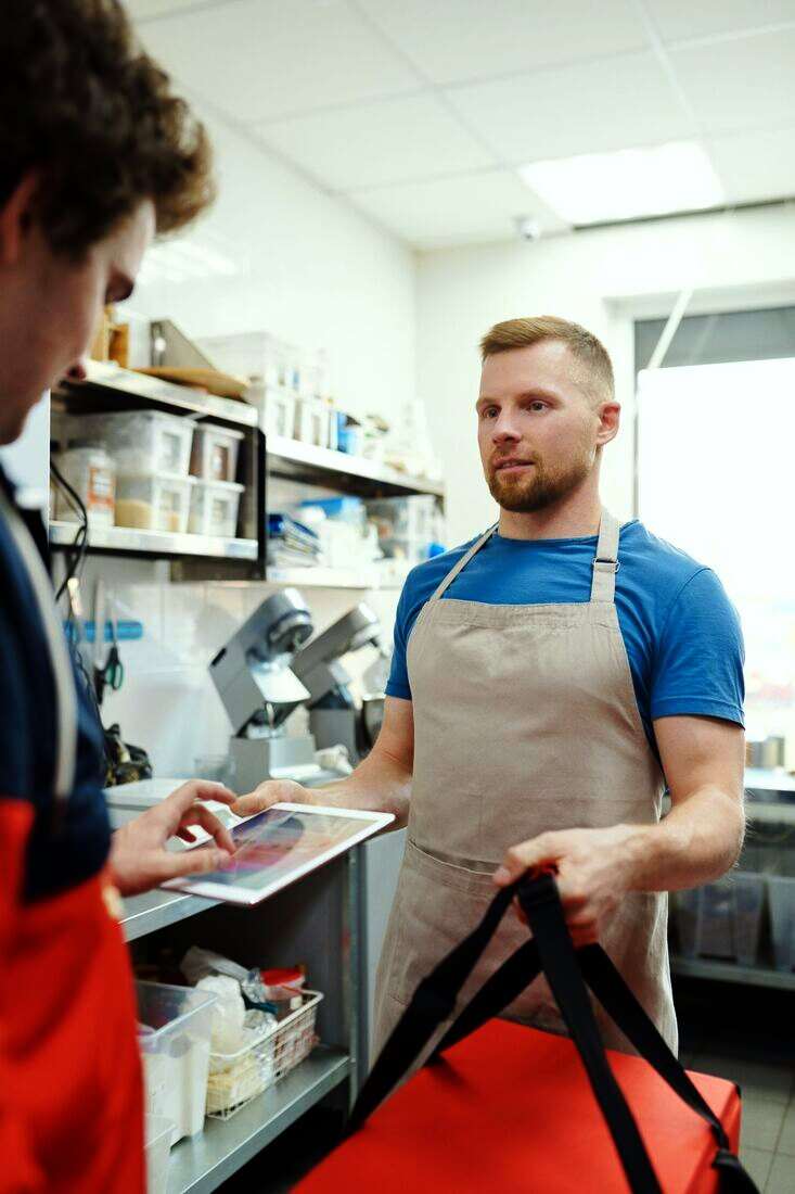 Dos ayudantes de cocina con delantal mirando una tablet