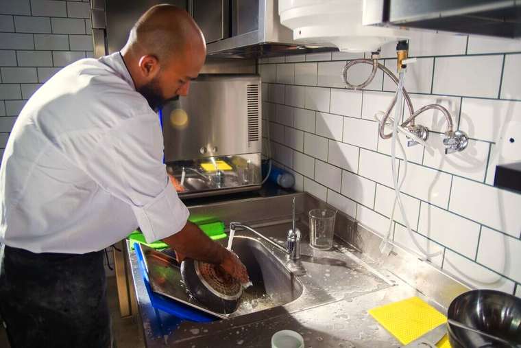 Ayudante de cocina lavando una sartén en la pileta