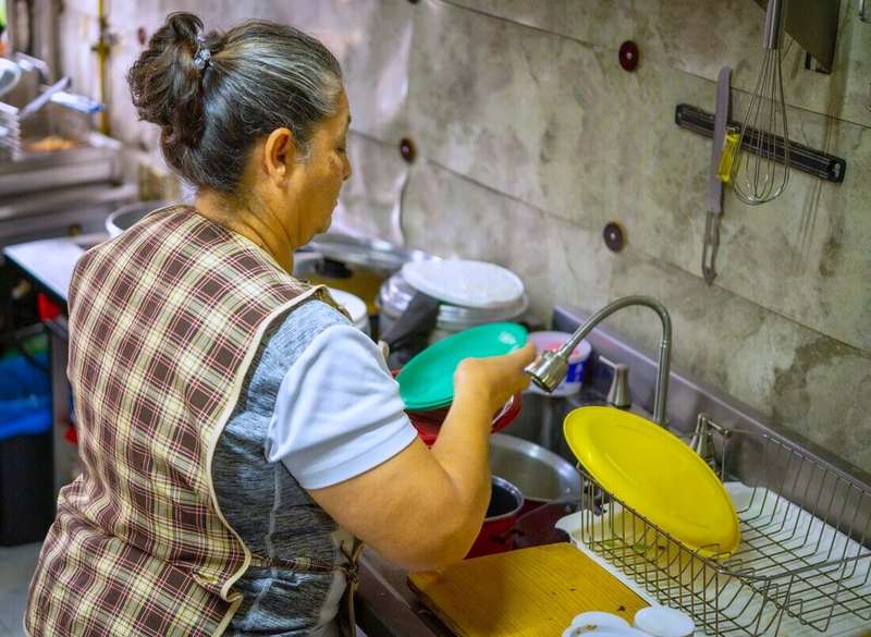 Mujer con delantal lavando platos en la pileta de una cocina
