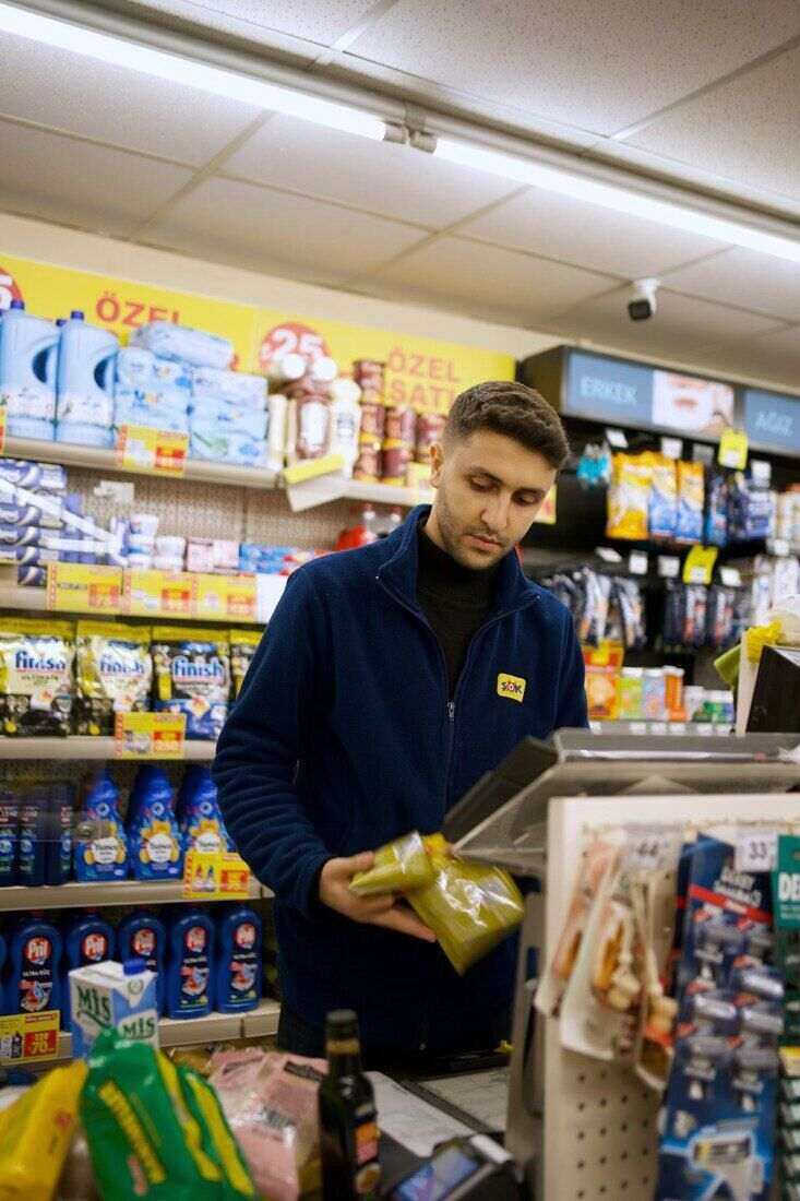 Empleado de un kiosco cobrando, con productos en las estanterías detrás