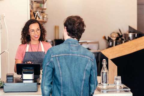 Empleada con delantal atendiendo a un cliente en la caja de un local