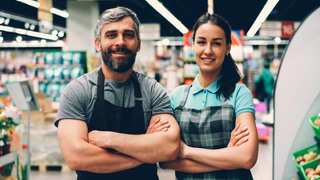 Dos empleados con delantal sonriendo con los brazos cruzados en un supermercado