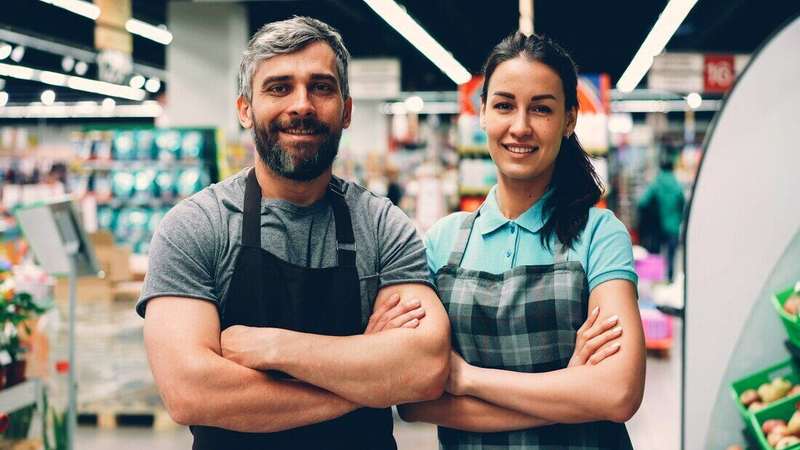 Dos empleados con delantal sonriendo con los brazos cruzados en un supermercado