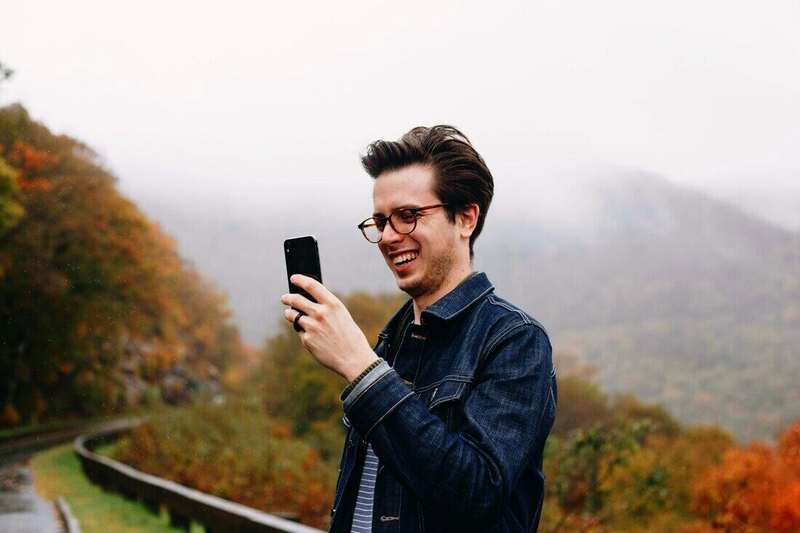 Hombre sonriendo mientras mira el celular al aire libre