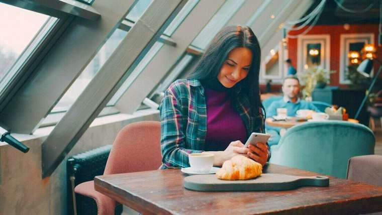 Mujer mirando el celular en un café luminoso