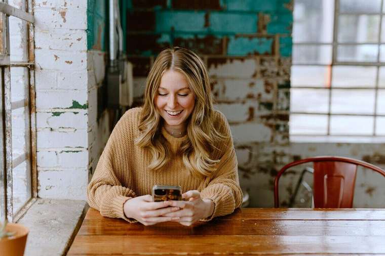 Mujer sonriendo mientras mira el celular en un café