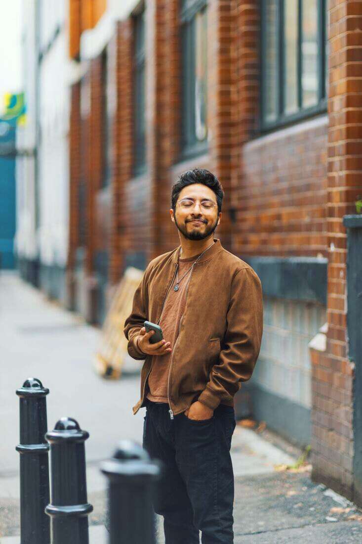 Hombre sonriendo con el celular en la mano en una vereda