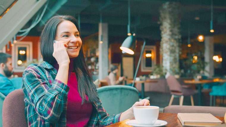 Mujer sonriendo mientras habla por celular en un café