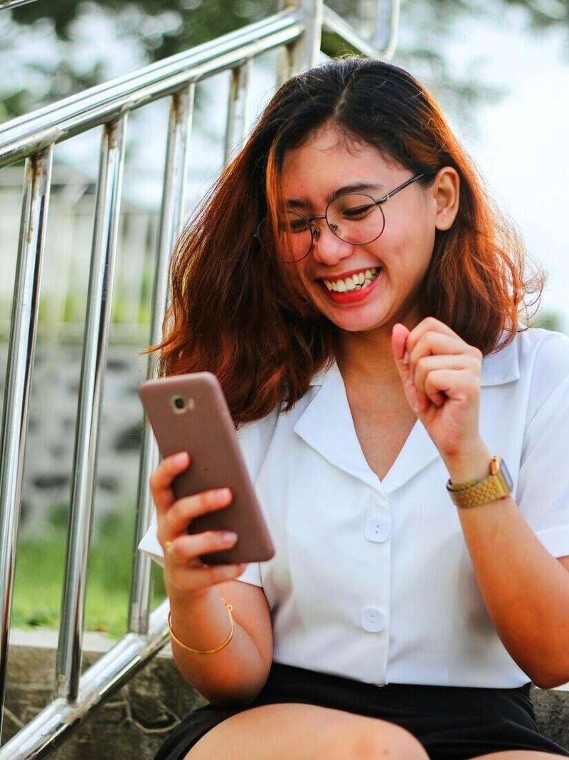 Mujer riendo mientras mira su celular