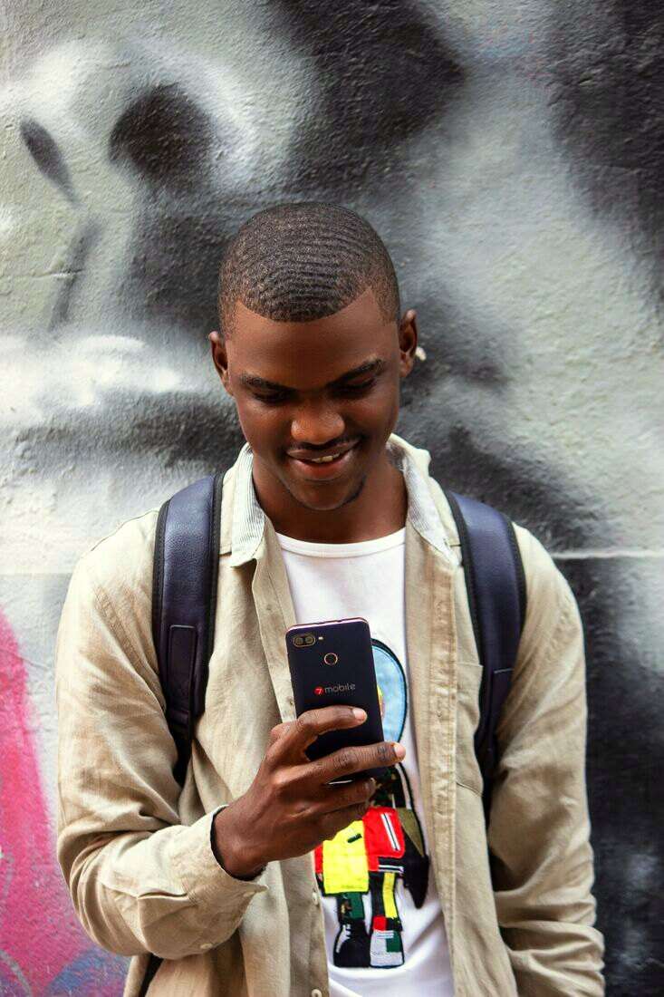 Hombre joven con mochila mirando el celular y sonriendo