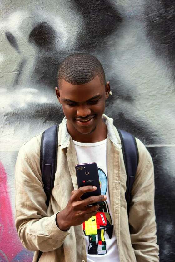 Hombre joven con mochila mirando el celular y sonriendo