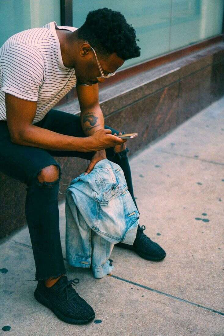 Hombre sentado en la vereda mirando el celular