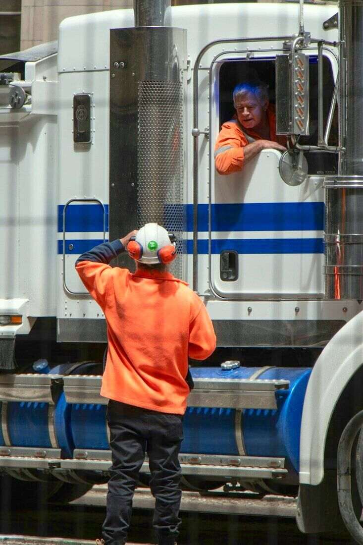 Hombre de espaldas con campera naranja junto a un camión