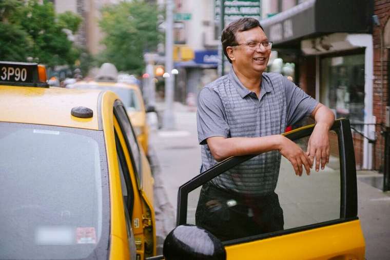 Hombre sonriendo con los brazos apoyados en la puerta abierta de un taxi amarillo
