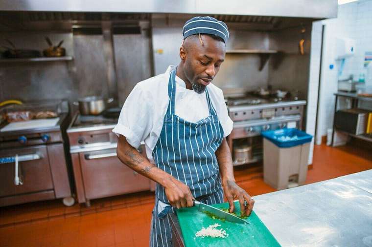 Cocinero con delantal cortando ajo en una cocina