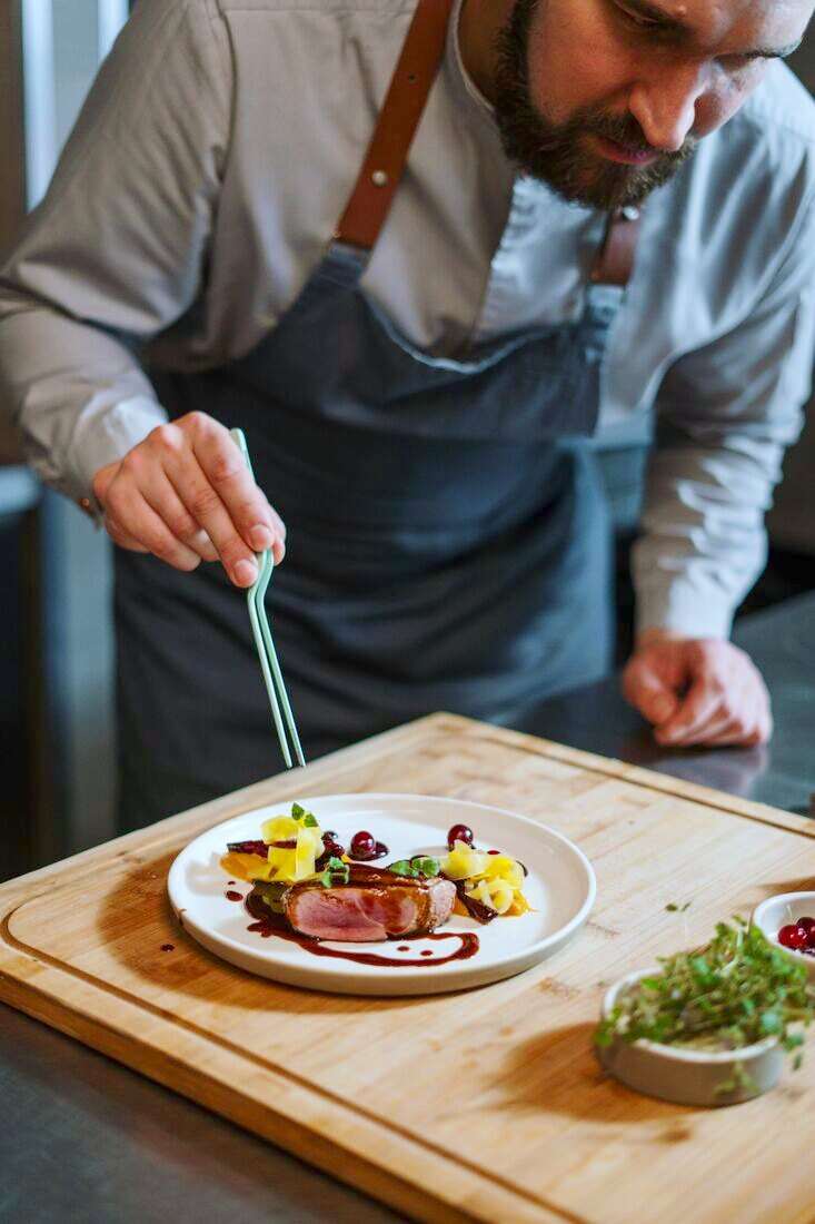 Cocinero con delantal emplatando un plato sobre una tabla de madera