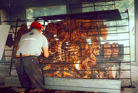 Parrillero acomodando cortes de carne sobre una parrilla grande con brasas