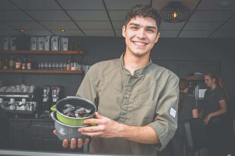Cocinero sonriendo con una cacerola en las manos en la cocina de un restaurante