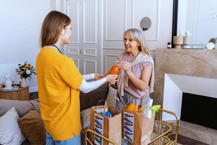 Mujer entregando bolsas de compras a una mujer mayor en su casa