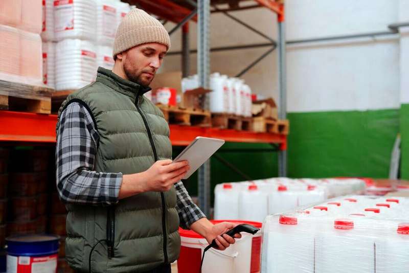 Empleado de depósito con una tablet y un lector de códigos junto a una estantería