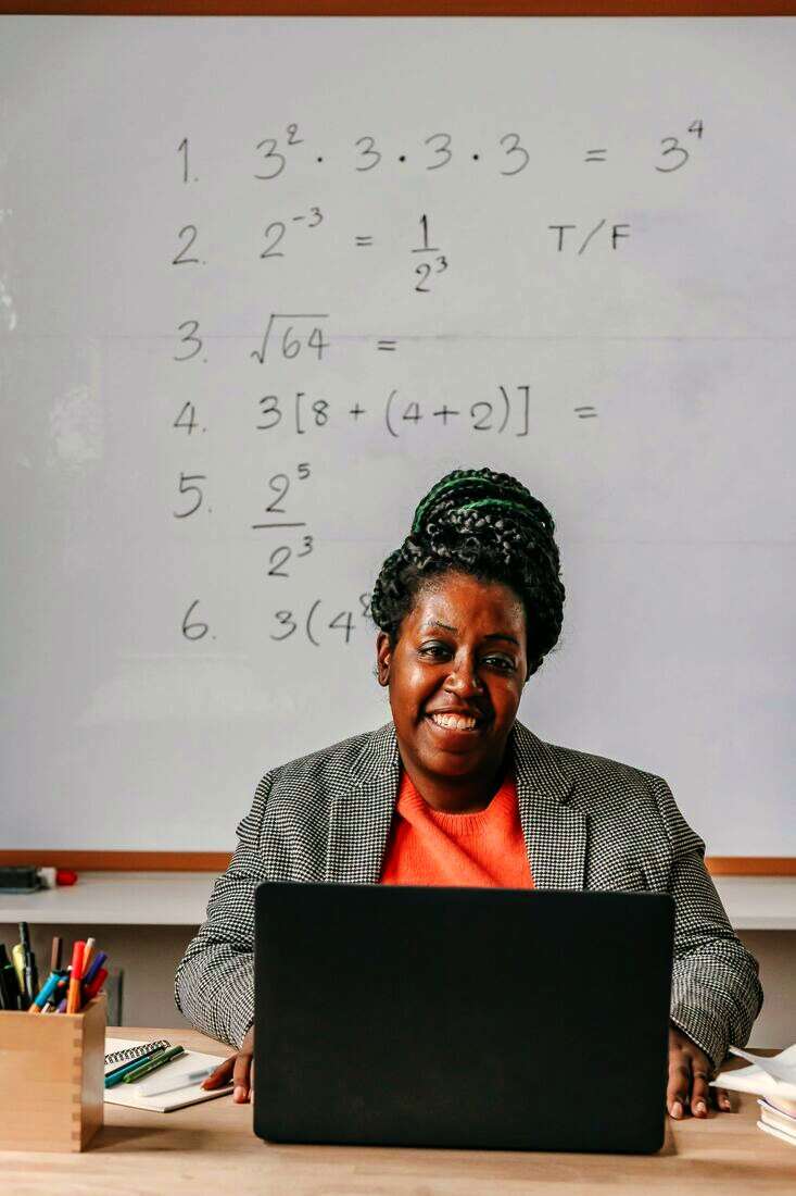 Docente sonriendo frente a una notebook y un pizarrón