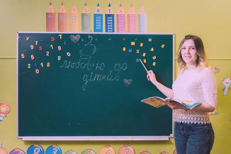 Docente señalando un pizarrón verde con letras de colores