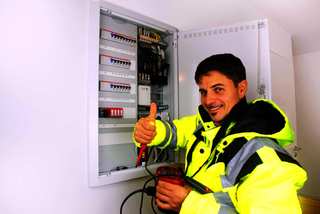 Electricista sonriendo con un tester junto a un tablero abierto