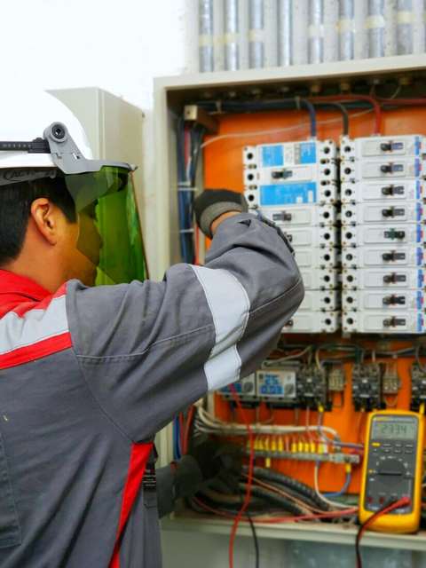Electricista industrial con visor y tester frente a un tablero