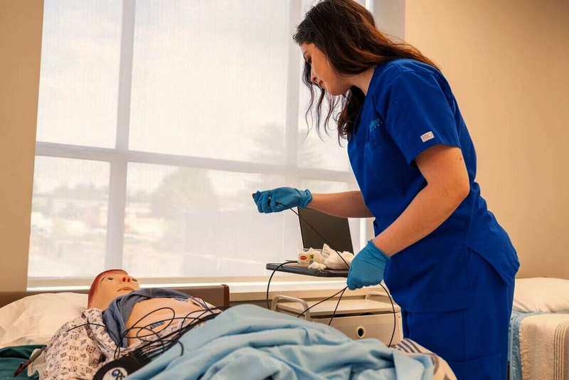 Estudiante de enfermería practicando con un maniquí en una sala de prácticas