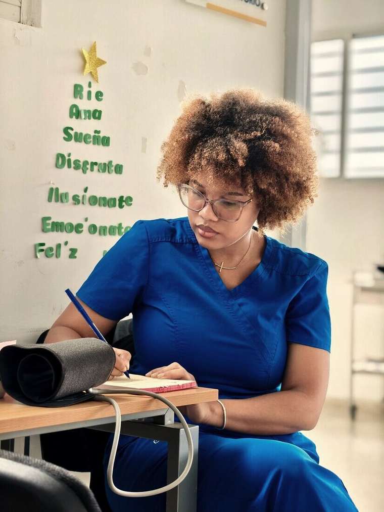 Enfermera anotando datos en un cuaderno junto a un tensiómetro
