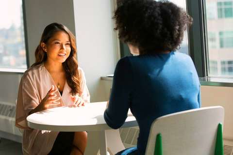 Dos mujeres conversando en una mesa blanca