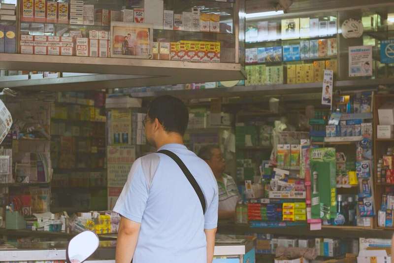Persona de espaldas frente al mostrador de una farmacia de barrio