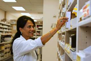 Farmacéutica con delantal blanco buscando un medicamento en un estante