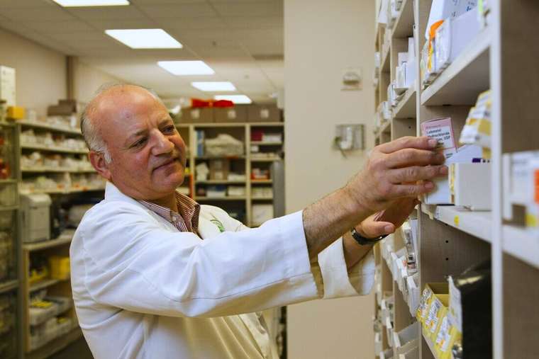 Farmacéutico con delantal blanco acomodando medicamentos en un estante