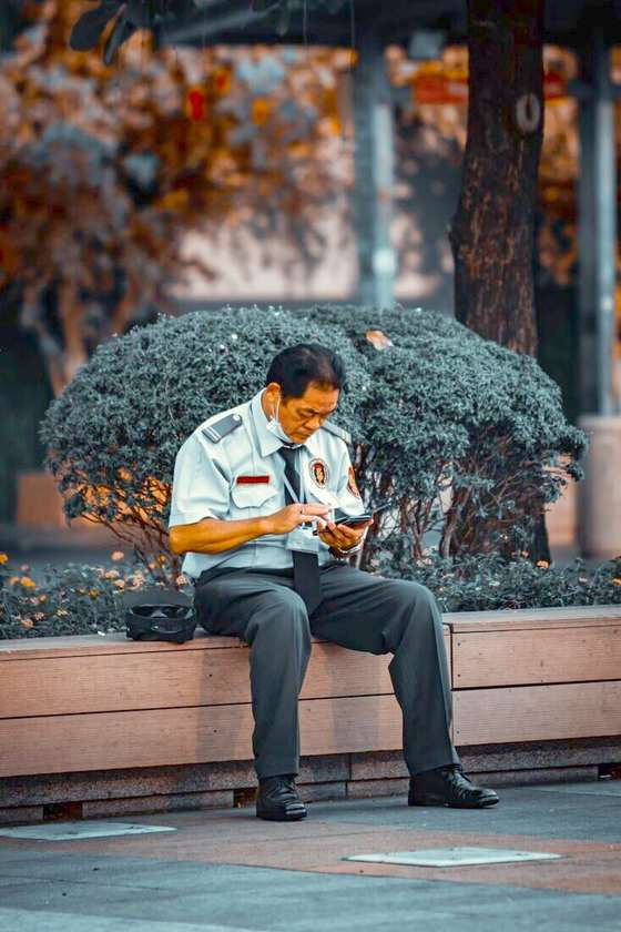 Guardia de seguridad sentado en un banco mirando su celular