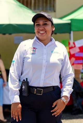 Guardia de seguridad sonriendo con camisa blanca y handy en un evento al aire libre