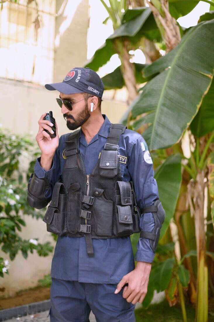 Guardia de seguridad con chaleco hablando por handy al aire libre