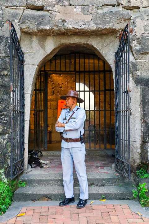 Guardia de uniforme claro de pie frente a la entrada con reja de un edificio
