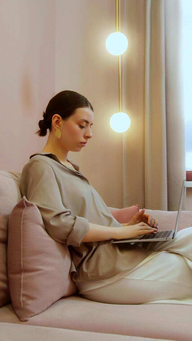 Mujer sentada en un sofá escribiendo en una notebook