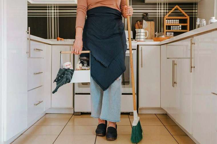 Mujer con delantal y escoba en una cocina