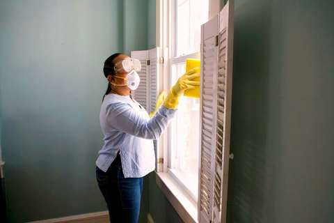 Mujer con barbijo y guantes limpiando una ventana en una casa