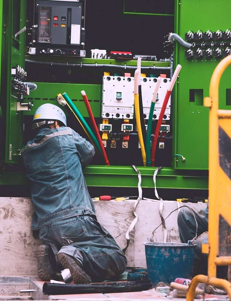Técnico con casco trabajando de rodillas en un tablero eléctrico