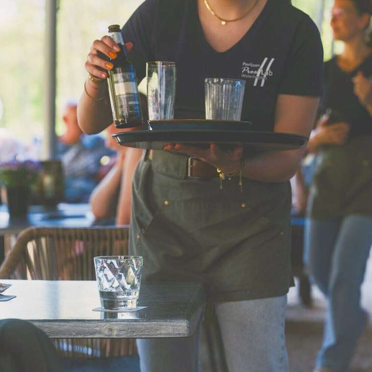 Moza llevando una botella y vasos en una bandeja