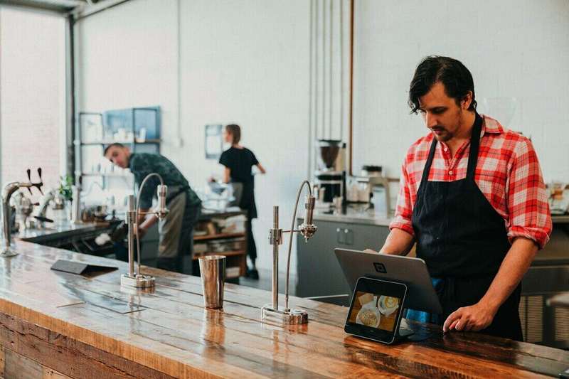 Hombre con delantal usando una tablet detrás de la barra de un café