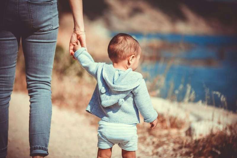 Adulta de espaldas llevando de la mano a un nene que camina
