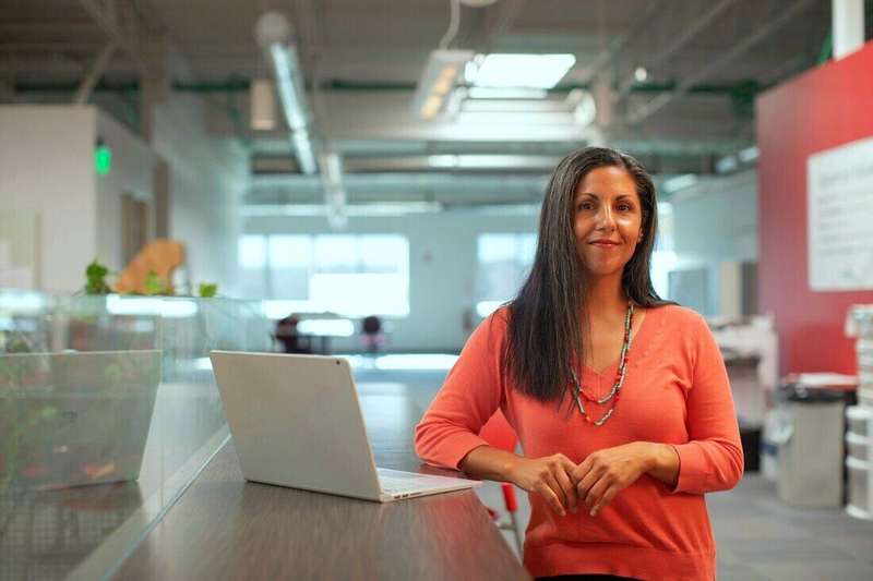 Mujer con blusa naranja de pie junto a una notebook en una oficina